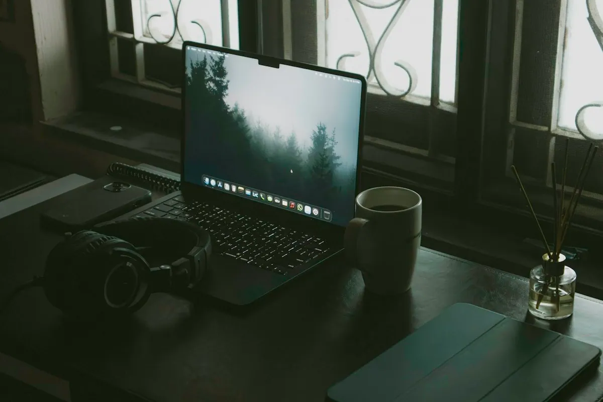 Laptop, headphones and coffee on a desk beside a window