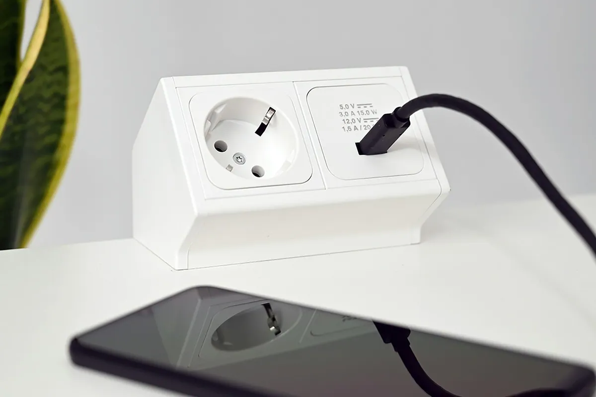 Phone charging at a white desk beside a small plant